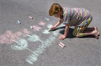 Girl paints flowers with chalk on asphalt