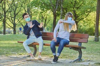 Man and woman wearing a face mask on a park bench in a municipal park