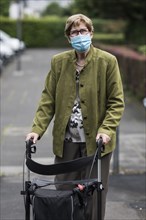 Senior citizen with mouth and nose protection and rollator on the street during Corona Pandemic