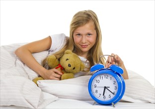 Girl with teddy and alarm clock in bed