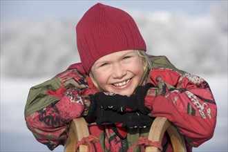 Little girl leaning on a sledge and laughing