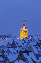 View over snowy roofs of the old town with illuminated church tower