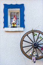 Garden gnomes at a small window and in a wooden wagon wheel