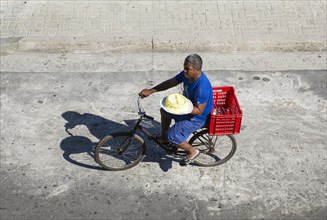 Man on a bicycle trying to sell a cake