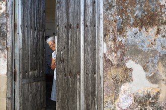 Woman at the entrance of her house with a decayed facade of crumbling plaster and a weathered wooden door