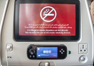 Screen with display smoking ban in Arabic and English on backrest in aircraft