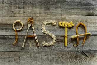 Word pasta from different noodles on wooden table