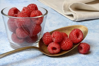 Raspberries in spoon and glass bowl