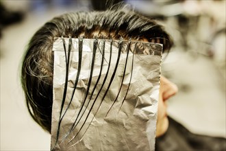 Hairdresser in a hairdressing salon dying strands of hair with aluminium foil