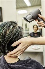 Hairdresser in a hairdressing salon blow-drying the dyed hair of a customer