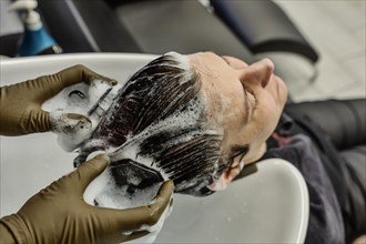 Customer in a hairdressing salon gets her hair washed with shampoo by a hairdresser