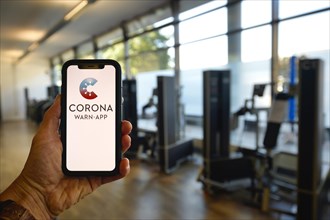 Hand holds smartphone with Corona Warn-APP in fitness center