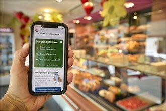 Hand holds smartphone with Corona Warn-APP in the bakery
