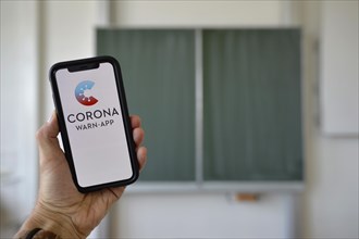 Hand holding smartphone with Corona Warning App in the classroom