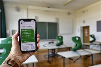 Hand holding smartphone with Corona Warning App in the classroom