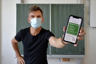 Teacher with face mask keeps smartphone with Corona Warning App in classroom