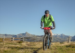 Mountain biker in his late forties rides on an ebike along an alpine path against a blue sky
