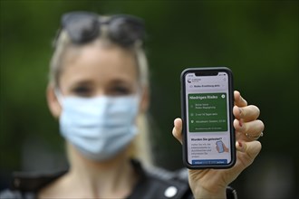 Woman with face mask shows smartphone with corona warning app