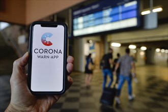 Hand holds smartphone with Corona Warn-APP in the train station