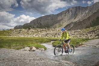 Mountain biker rides on alpine gravel road through mountain river