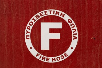 Close-up of red and white painted metal cabinet cover with Fire Hose written in Greek and English languages