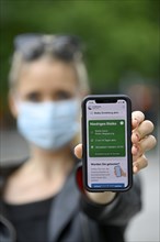 Woman with face mask shows smartphone with corona warning app