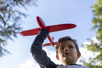 A boy plays with a red toy plane