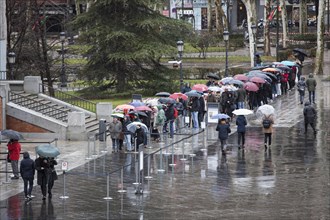 Tourists from abroad stand by the line with their umbrellas to get a ticket for a visit to the Prado Museum on a rainy sunday in Madrid