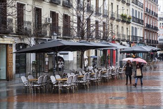 Empy seats in terraces of chueca square in the gay district as people walks by on a rainy day