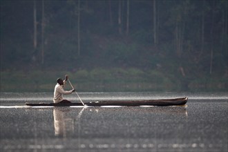 Man paddling in dugout canoe on a lake
