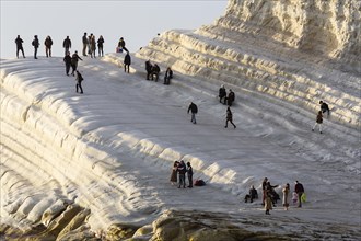 Tourists hiking on chalk cliffs Scala dei Turchi in the evening