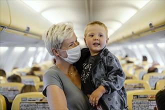 Mother wearing mask holding 2 years old son in the airplane