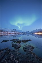 Aurora borealis above snow-covered peaks reflected in a fjord