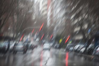 A blurry image of the street with cars and traffic lights taken from inside the car during a rainy day in Madrid