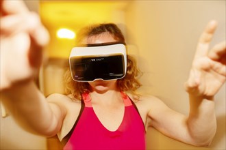 Young woman with VR glasses reaches for the air at home