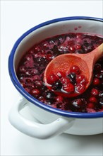 Boiled red and black currants in bowl with wooden spoon