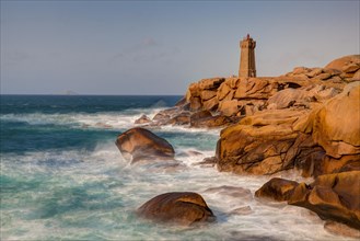 Lighthouse on red granite rocks and rough sea