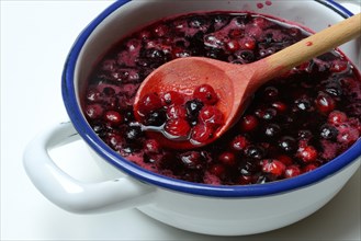 Boiled red and black currants in bowl with wooden spoon
