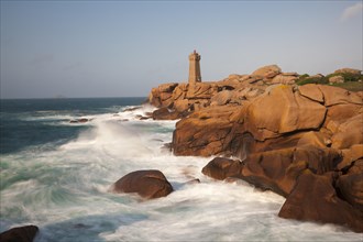 Lighthouse on red granite rocks and rough sea