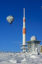 Hot-air balloon with transmitter mast and Brocken hostel on the winter snow-covered Brocken