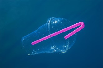 A plastic cocktail cup with a straw floats slowly under water in blue water