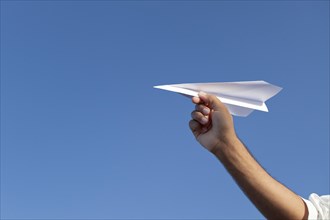 Hand holding paper airplane in front of blue sky