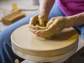 Potter turning a vase with her hands on the potter's pane