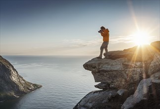 Photographer in front of sun on rocky outcrop