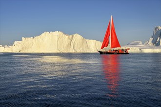 Red sailing boat in front of icebergs