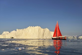 Red sailing boat in front of icebergs