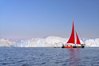 Red sailing boat in front of icebergs at the blue hour