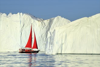 Red sailing boat in front of gigantic icebergs