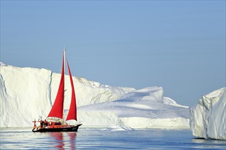 Red sailing boat in front of gigantic icebergs
