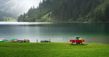 Couple with umbrella sitting in the rain at Vilsalpsee in Tyrol